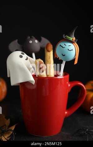 Verschiedene Kuchenwürfel im Becher, dekoriert als Monster auf dem schwarzen Tisch. Halloween-Leckerbissen Stockfoto