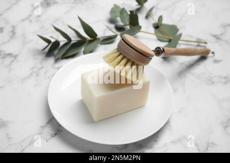 Reinigungsbürste und Seifenleiste zum Geschirrspülen auf weißem Marmortisch Stockfoto
