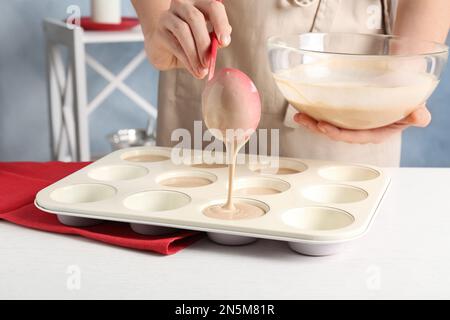 Eine Frau, die Teig in ein Cupcake-Tablett am weißen Tisch in der Küche gießt, Nahaufnahme Stockfoto