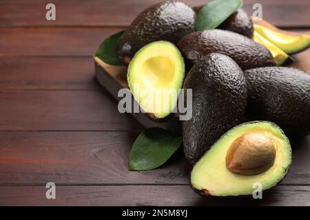 Ganze und geschnittene Avocados auf einem Holztisch. Platz für Text Stockfoto