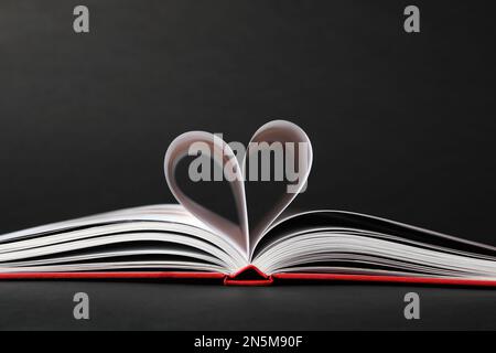 Offenes Buch mit im Herzen gefalteten Seiten auf schwarzem Hintergrund Stockfoto