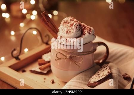 Leckeres heißes Getränk mit Schlagsahne und Weihnachtslichtern auf dem Tisch, Nahaufnahme Stockfoto