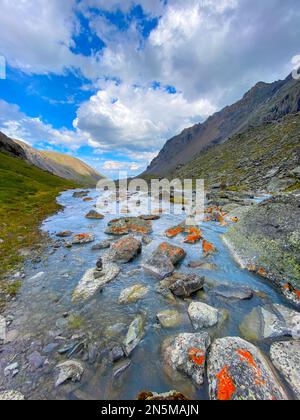 Ein kleiner Bach fließt zwischen orangefarbenen Felsen in Richtung eines Felsens in Altai, Sibirien. Stockfoto