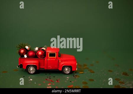 Roter Spielzeugwagen mit Weihnachtsbällen und Tannenzweig im Kofferraum. Miniaturwagen mit Weihnachtsdekoration auf grünem Hintergrund. Helle Kulisse mit Spa Stockfoto