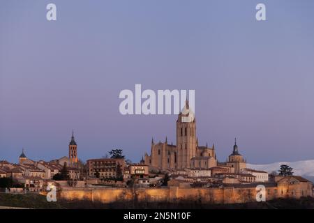 Segovia, Spanien - 4. Januar 2022: Panoramablick auf Segovia mit den Türmen der Kathedrale bei Sonnenuntergang und violettem Himmel im Winter mit dem Guadarrama-Gebirge Stockfoto