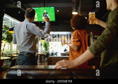 Eine Gruppe von Freunden, die sich das Fußballspiel auf dem fernsehbildschirm in der Sportbar anschauen Stockfoto