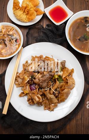 Gebratene Nudeln mit Gemüse und Rindfleisch in weißer Schüssel auf braunem Holz Stockfoto