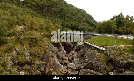 Eine Brückenstraße, die die grün bedeckten Gebiete verbindet, durch die ein Fluss in Sirdal, Norwegen fließt Stockfoto