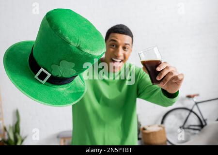 Glücklicher afroamerikanischer Mann mit einem Glas dunklem Bier und grünem Hut am Saint Patrick Day Stockfoto