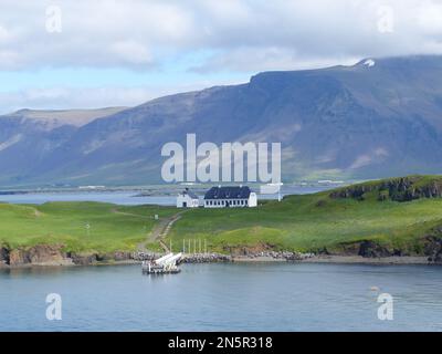 Eine Landschaftsszene mit ländlichen Häusern auf Videy Island mit grünen Bergen und verschwommenem Himmel Stockfoto