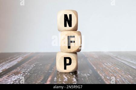 Drei Holzwürfel mit Buchstaben - nfp auf gelbem Tisch, Platz für Text rechts. Vorderansicht, Blume im Hintergrund. nfp – Abkürzung für Non-FAR Stockfoto