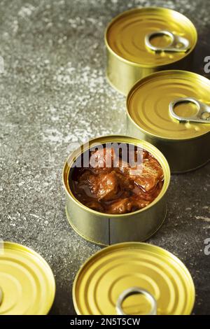 Geschlossene runde kleine Dosen, außer einer mit Tintenfischstücken in Sauce auf einer grauen Oberfläche Stockfoto