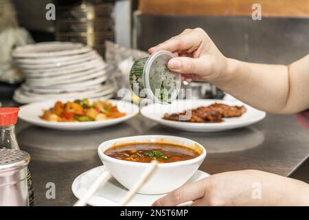 Eine Kellnerin im chinesischen Restaurant garniert eine Suppe mit Schnittlauch in einer weißen Schüssel und bringt sie an einen Tisch Stockfoto