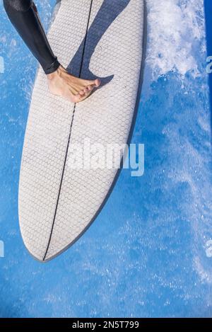 Ein Surfer auf seinem Brett, der auf dem Wappen der Welle reitet und das morgendliche Sonnenlicht empfängt Stockfoto