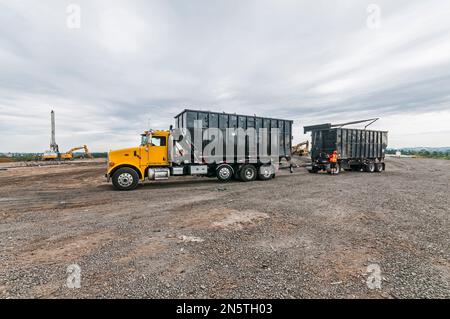 Ein Arbeiter, der auf einer aktiven Deponie in einem Sattelzugmaschine mit Bohrlochbohrer und Schaufel arbeitet. Stockfoto