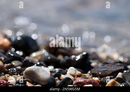 Nasse Kieselsteine auf verschwommenem Hintergrund von Meereswellen. Strandurlaubskonzept Stockfoto