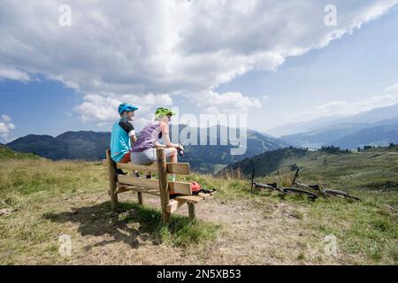 Junges Paar Mountainbiker sitzen auf Bank in alpiner Landschaft, Zillertal, Tirol, Österreich Stockfoto