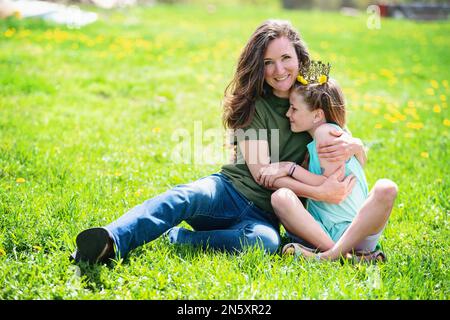 Mutter umarmte blonde Tween-Tochter mit Löwenzahn-Krone. Stockfoto