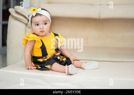 Baby-Latina, sitzt und sieht merkwürdig weg, trägt ein gelbes Kleid. Stockfoto