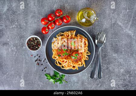 Hausgemachte Spaghetti mit Tomatensoße, Fleischklößchen und Gewürzen, serviert auf schwarzem Teller auf grauem Betonhintergrund. Leckere gekochte Pasta mit Hackfleisch Stockfoto