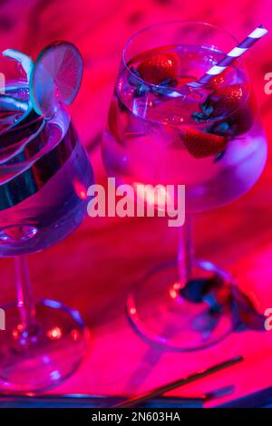 Nahaufnahme von Gläsern mit Wasser und Obst auf Holzbrett über Neonlichtern Stockfoto