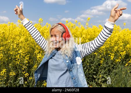 Ältere Frauen hören Musik mit Kopfhörern im blühenden Rapsfeld Stockfoto