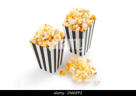 Zwei schwarz-weiß gestreifte Eimer mit leckerem Käsepopcorn, isoliert auf weißem Hintergrund. Film-, Kino- und Unterhaltungskonzept.