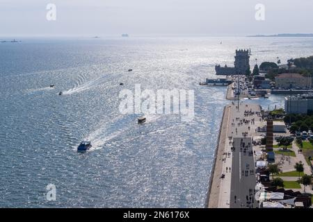 Luftaufnahme der Flussmündung des Tejo in Belem, Lissabon, Boote auf dem Fluss, entfernte Menschen auf dem Fußweg und der Turm von Belem hinten Stockfoto