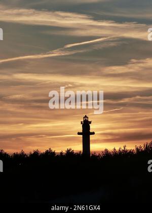 Eine vertikale Silhouettenaufnahme einer Säule und Vegetation mit einer Wolkenlandschaft bei Sonnenuntergang im Hintergrund auf der Insel Bornholm Stockfoto