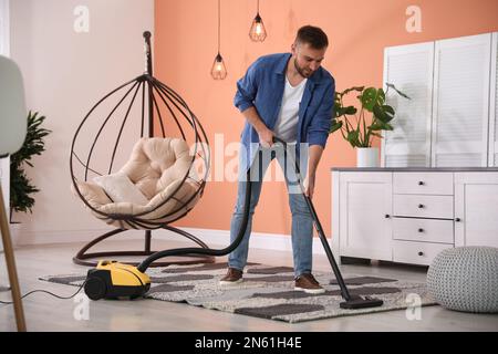 Junger Mann, der zu Hause Staubsauger benutzt Stockfoto