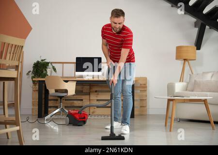 Junger Mann, der zu Hause Staubsauger benutzt Stockfoto