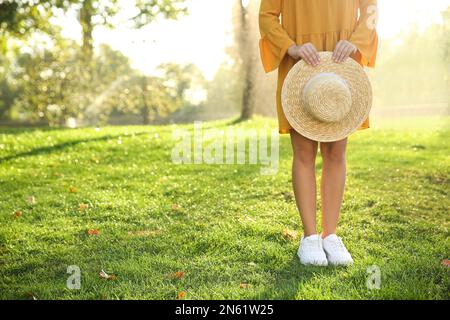 Eine Frau trägt ein stilvolles gelbes Kleid und Turnschuhe mit Strohhut im Park, Nahaufnahme Stockfoto