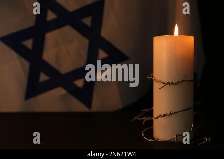Stacheldraht und brennende Kerze auf schwarzem Hintergrund. Holocaust-Gedächtnisfeiertag Stockfoto