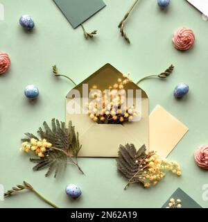 Ostern-Hintergrund. Mimosa- und Freesia-Blumen, Wachteleier, mintgrüne Umschläge und Farbpapier auf grünem Hintergrund. Flach liegend, über Kopf, knurrt Stockfoto