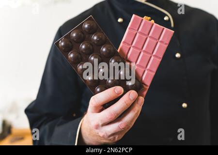 Nahaufnahme einer männlichen Konditorhand mit zwei handgefertigten Schokoriegeln. Hochwertiges Foto Stockfoto