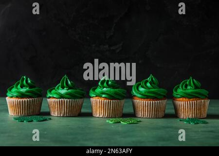 Leckere Cupcakes für St. Patrick's Day auf grünem Tisch vor schwarzem Hintergrund Stockfoto