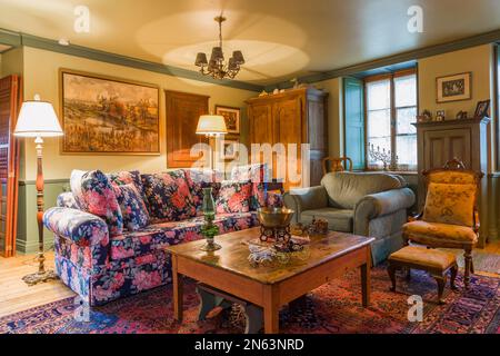 Couchtisch aus Pinienholz mit farbenfrohen Blumenmustern, grünem Polstersessel, Sitzsessel mit Kissen und Holzschrank im Wohnzimmer. Stockfoto