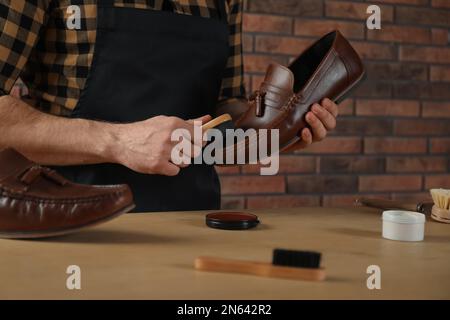 Handwerker, der sich professionell um braune Lederschuhe kümmert, in der Werkstatt, Nahaufnahme Stockfoto