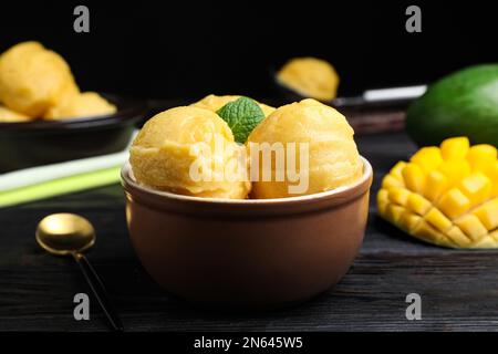 Leckeres Mangoeis in der Schüssel auf einem schwarzen Holztisch Stockfoto