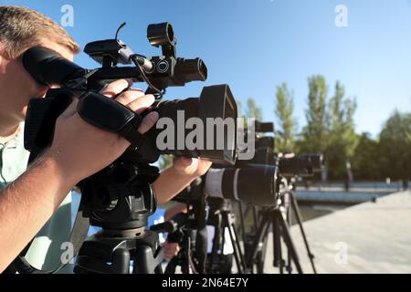 Mitarbeiter mit professionellen Videokameras arbeiten an sonnigen Tagen im Freien Stockfoto