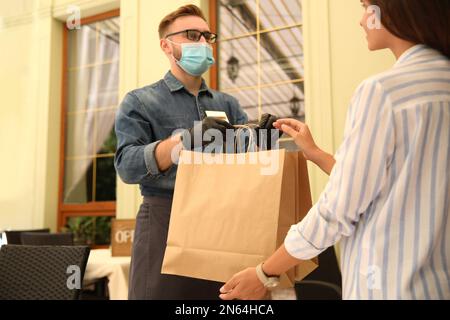 Der Kellner gibt dem Gast im Restaurant eine Bestellung zum Mitnehmen. Gastronomie während der Coronavirus-Quarantäne Stockfoto