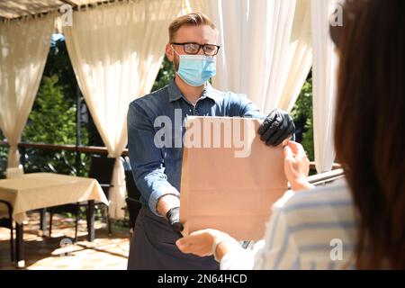 Der Kellner gibt dem Gast im Restaurant eine Bestellung zum Mitnehmen. Gastronomie während der Coronavirus-Quarantäne Stockfoto