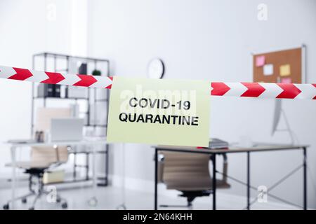 Blatt Papier mit den Worten COVID-19 Quarantine auf rotem und weißem Band im Büro Stockfoto
