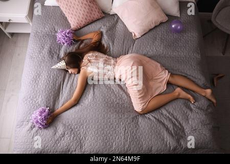 Erschöpfte Frau in festlichem Outfit, die zu Hause nach der Party im Bett schläft, über der Aussicht Stockfoto