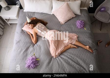 Erschöpfte Frau in festlichem Outfit, die zu Hause nach der Party im Bett schläft, über der Aussicht Stockfoto