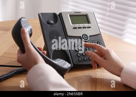 Frau, die Tischtelefon am Holztisch im Büro benutzt, Nahaufnahme. Hotline-Service Stockfoto