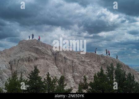 Interior, SD, USA - 20. Juni 2022: Touristen erklimmen einen kleinen Hügel im Badlands-Nationalpark, während Sturmwolken aufrollen. Stockfoto