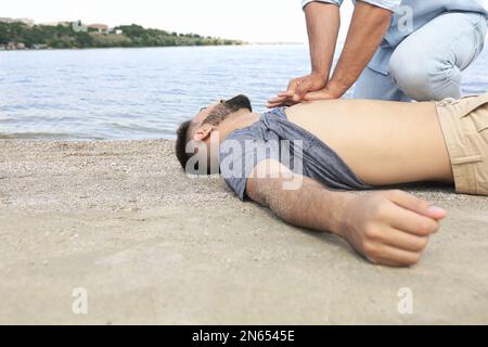 Passanten, die eine Wiederbelebung an bewusstlosen jungen Mann auf See durchführen. Erste Hilfe Stockfoto