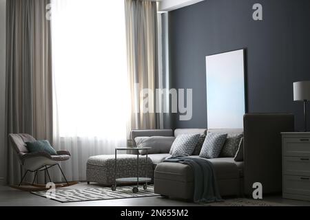 Komfortables Sofa und Schaukelstuhl in Fensternähe mit eleganten Vorhängen im Zimmer Stockfoto