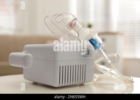 Moderner Vernebler mit Gesichtsmaske auf weißem Tisch im Innenbereich. Inhalationsgeräte Stockfoto